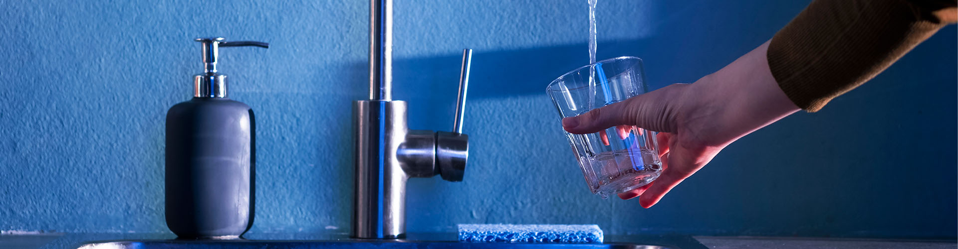 Photo d'une main tenant un verre d'eau en train de se remplir sous un robinet